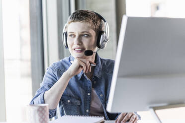 Businesswoman wearing headset at desk in office - UUF21179