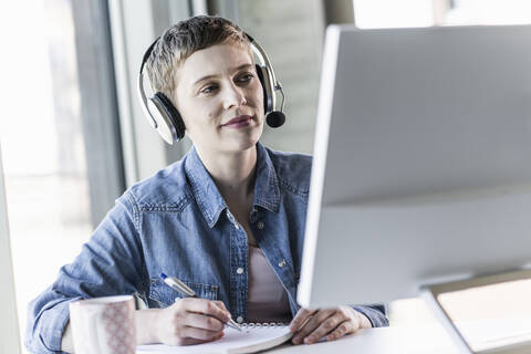 Businesswoman wearing headset at desk in office taking notes stock photo