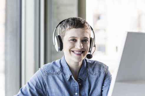 Porträt einer lächelnden Geschäftsfrau mit Headset am Schreibtisch im Büro - UUF21184