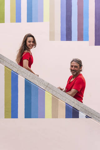 Lächelnder Vater und Tochter stehen auf einer bunten Treppe an einem sonnigen Tag, lizenzfreies Stockfoto