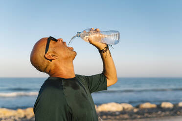 Senior man drinking water while standing against clear sky - EGAF00687