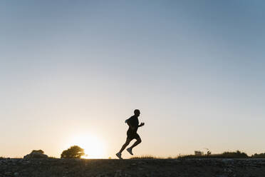 Silhouette eines älteren Sportlers beim Joggen gegen den klaren Himmel bei Sonnenuntergang - EGAF00689