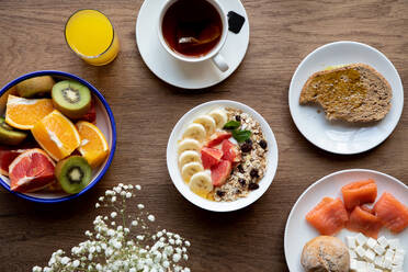 Von oben Schale Müsli mit leckeren Beeren und Banane serviert auf dem Tisch mit Teller mit Obst und Tee Tasse mit zum Frühstück - ADSF14458