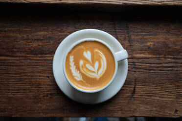 Von oben Tasse frischer Cappuccino mit Herzform auf Schaum serviert auf Holztisch in Cafe - ADSF14460