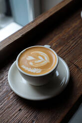 From above cup of fresh cappuccino with heart shape on froth served on wooden table in cafe - ADSF14461