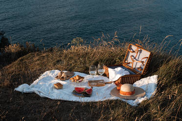 Picknickmatte mit romantisch mit einem Glas Getränk und Essen auf trockenen Ufer mit ruhigen Wasser und Hügeln gesetzt - ADSF14496