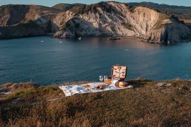 Picknickmatte mit romantisch mit einem Glas Getränk und Essen auf trockenen Ufer mit ruhigen Wasser und Hügeln gesetzt - ADSF14497