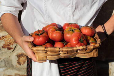 Tasty appetizing tomatoes with green stems in brown straw-plaited basket in hands - ADSF14510