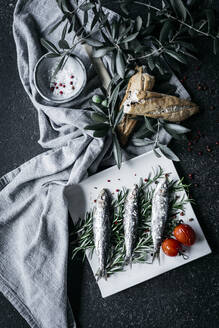 Salted anchovies placed on heap of rosemary sprigs near fabric napkin with olive branches and fresh bread - ADSF14551