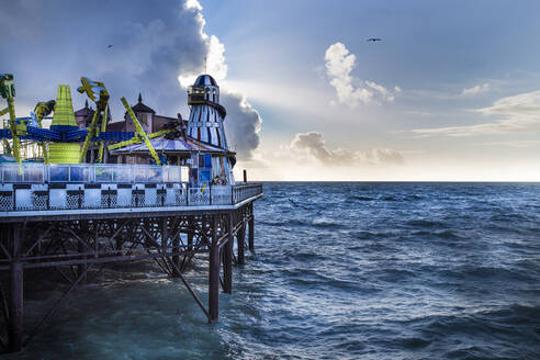 Bunte Attraktionen des Vergnügungsparks auf dem Pier in der Nähe von wogenden Meer gegen bewölkten Himmel am Abend in Brighton, England - ADSF14599