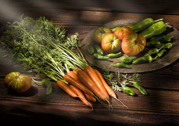 Karotte mit üppigen grünen Stängeltomaten, Paprika auf rundem Tablett und Kohl in Körben auf Holztisch in warmem Kontrastlicht - ADSF14601
