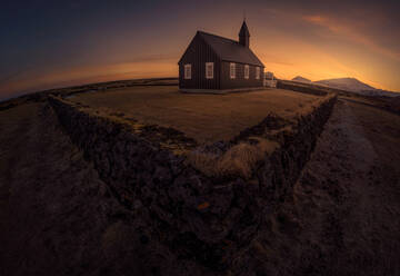 Einfaches Kirchengebäude hinter altem Steinzaun vor hellem Sonnenuntergangshimmel in Island - ADSF14619