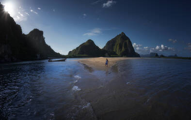 Unrecognizable traveler standing near waving sea water and mountains on sandy coast on sunny day in Thailand - ADSF14622