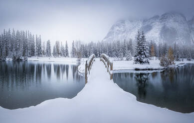 Schöne kanadische Winterlandschaft mit schneebedeckten Brücke über ruhiges Wasser mit Tannenwald und nebligen schneebedeckten Bergen im Hintergrund - ADSF14627