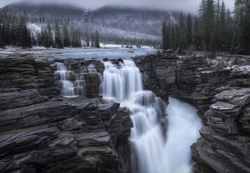 Spektakuläre Landschaft mit wunderschönem Wasserfall inmitten felsiger, mit Nadelwald und Schnee bedeckter Berge in Kanada - ADSF14628