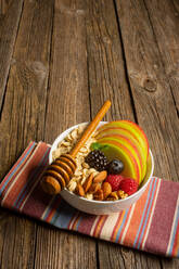 From above of bowl with nuts fruit and berries healthy food with honey dipper on cloth on wooden table - ADSF14644