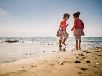 Cheerful cute twins playing on sandy seashore on background of clear sky - ADSF14654