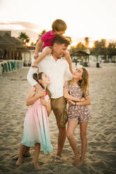 Adult man with laughing boy on shoulders standing with beautiful little girls on beach spending time together - ADSF14672