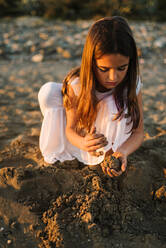 Cute nachdenklich weiblichen Kind in weißem Kleid spielen mit Sand am Meer im Sonnenlicht - ADSF14679