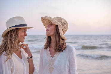 Smiling girlfriends in summer clothes barefoot in water on beach - ADSF14686