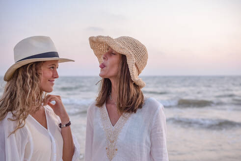 Lächelnde Freundinnen in Sommerkleidung barfuß im Wasser am Strand - ADSF14686