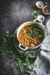 Draufsicht auf eine Schüssel mit köstlichem veganem Kichererbsencurry mit Kräutern, die neben einer Stoffserviette auf einer grauen Tischplatte steht - ADSF14692