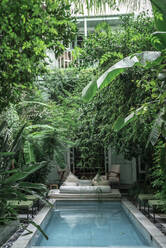 Schwimmbad und Liege inmitten grüner exotischer Pflanzen vor dem Hotelgebäude in Marrakesch, Marokko - ADSF14708