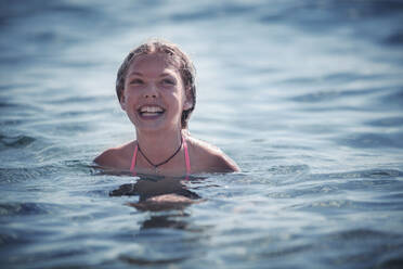 Lächelndes Mädchen beim Schwimmen im Meer im Sommer - DHEF00344