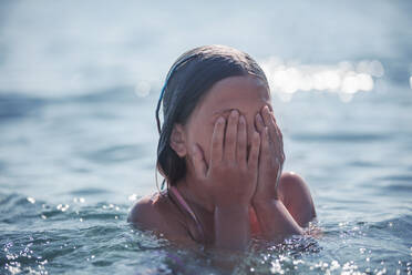 Mädchen bedeckt ihr Gesicht mit der Hand, während sie im Sommer im Meer spielt - DHEF00346