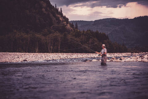 Fly fisherman casting with fishing rod while standing in river stock photo