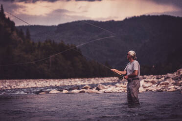 Fly fisherman casting with fishing rod while standing in river - DHEF00355