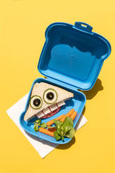 Lunch box with baby carrots and funny looking sandwich with anthropomorphic face - GEMF04131