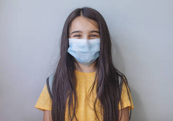 School girl with face mask standing against gray wall - MOMF00909