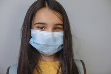 Girl with protective face mask standing against gray wall - MOMF00910