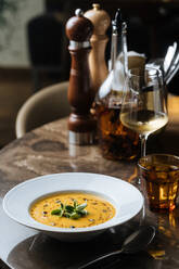 Von oben schmackhafte appetitliche Gemüsecremesuppe in weißem Teller serviert mit Wein im Glas am Tisch im Cafe - ADSF14728