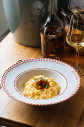 Von oben appetitliches Risotto mit Kürbis, dekoriert mit geschnittenen Tomaten und Grün in dekorativem Teller auf dem Tisch - ADSF14730