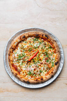 Draufsicht auf eine runde Pizza mit Tomatensoße und geschmolzenem Käse, garniert mit gehacktem grünem und einfachem Cayennepfeffer - ADSF14761