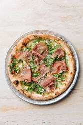 Draufsicht auf eine leckere Pizza mit dünnen Speckscheiben und frischem Grün auf einem Teller im Restaurant - ADSF14762