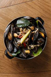 Top view of black mollusk dish with assorted steamed vegetables in black pot on table - ADSF14763