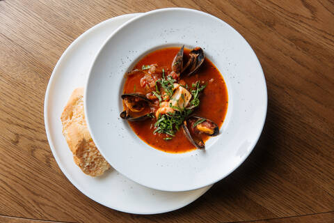 Top view of white round plate with rich spicy tomato soup with black mussels and seafood garnished with chopped greens stock photo