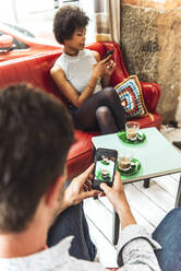 Man photographing coffee served on table while girlfriend using smart phone in cafe - EHF00788