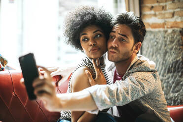 Paar spitzt die Lippen, während es ein Selfie mit dem Smartphone macht, während es im Café sitzt - EHF00796