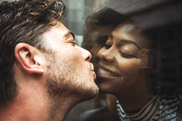 Close-up of romantic man kissing girlfriend through glass window - EHF00829