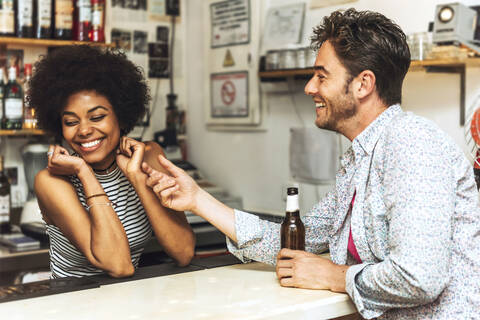 Mann berührt fröhliche Barkeeperin beim Flirten mit ihr am Bartresen, lizenzfreies Stockfoto