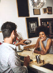 Smiling woman looking at male bartender preparing cocktail on bar counter - EHF00846