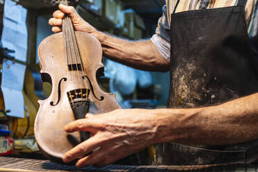 Violin maker examining violin for repairing at workshop - JCMF01215