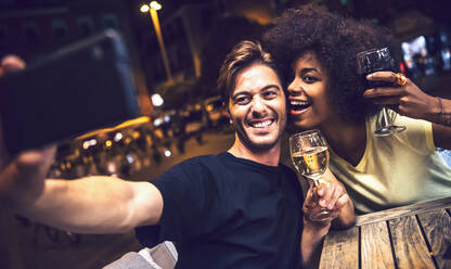 Cheerful couple holding wineglasses taking selfie at date night - EHF00855