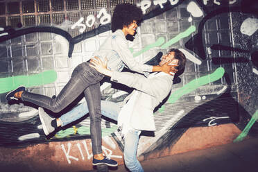 Carefree couple dancing against graffiti wall at night - EHF00861