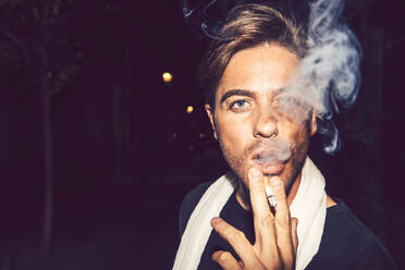 Nahaufnahme eines gut aussehenden Mannes, der nachts im Freien eine Zigarette raucht - EHF00886
