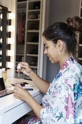 Smiling young female looking at cosmetic serum while sitting at home - JMHMF00088